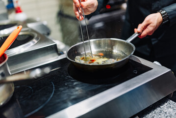man chef cooking fried shrimp in frying pan on kitchen
