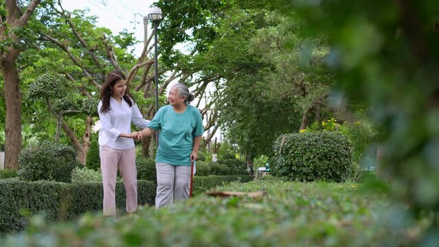 An old elderly Asian woman uses a walker and walking in the garden with her daughter.  Concept of happy retirement With care from a caregiver and Savings and senior health insurance, health care