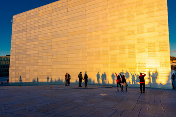 Tourists having fun with their shadows at the Oslo opera house at sunset - obrazy, fototapety, plakaty
