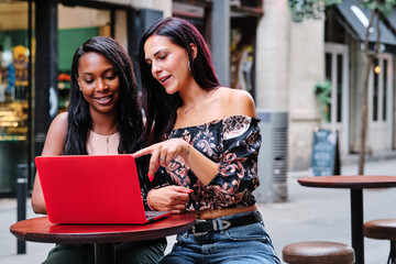 Lesbian couple using a laptop in a cafeteria terrace