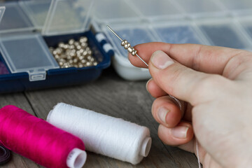 Female hands making of handmade jewellery. Box with beads, spool of threads, needle on wooden...