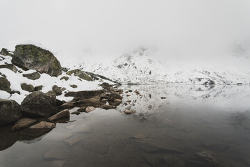 Panorama na staw w Tatrach Polskich w zimowej aurze z dużą ilością śniegu. Mglista pogoda