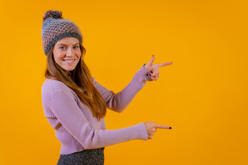 Woman with wool cap on a yellow background pointing to the right smiling, advertising concept