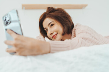 Beautiful Asian Korean woman taking selfie with smartphone or mobile phone on bed.
