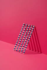 Blue striped paper straws leaning on magenta wall. Minimal concept.