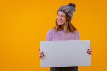 Woman in a wool cap holding a white billboard on a yellow background, advertisement