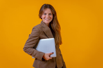 Fototapeta premium Portrait of a businesswoman with a computer on a yellow background, young entrepreneur concept