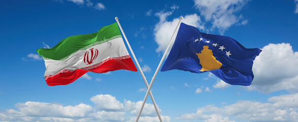 two crossed flags Kosovo and Iran waving in wind at cloudy sky. Concept of relationship, dialog, travelling between two countries