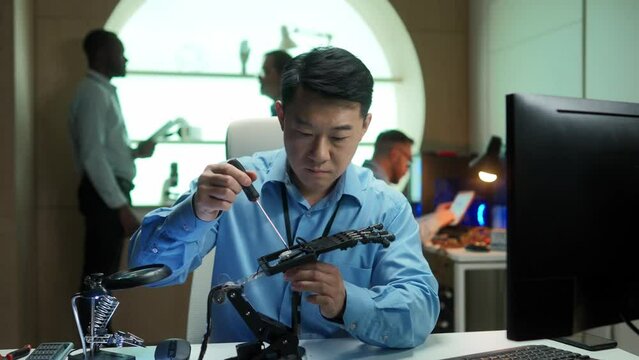 Portrait of successful professional asian man building and setting robotic hand prosthesis using tools. Handsome smart male engineer working in modern company office. Technologies concept.