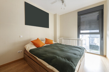 Bedroom with a double bed on a wooden sofa with drawers, a duvet, a cot in a corner and a narrow balcony
