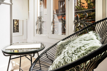 Reading corner on a closed balcony with aluminum and glass windows with an armchair with cushions and a matching circular table