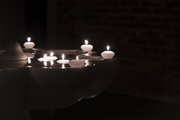 Floating wax candles burning in a marble fountain in the dark