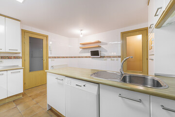 Island of a conventional kitchen with white wooden cabinets with steel handles and white integrated appliances
