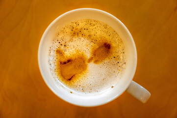 Cup of coffee on a table seen from above. Cafe latte macchiato with coffee marks on the top of the drink and bubbles in the foam.