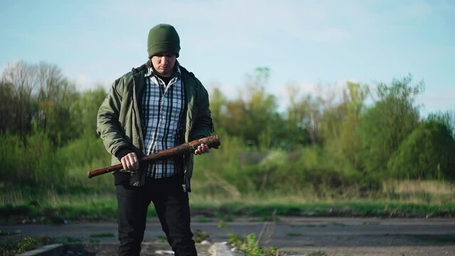 The man has a big wooden baseball bat in his hands. Shooting from outside the city on a vacant lot