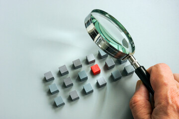 Talent management concept. A hand with a magnifying glass over gray cubes and one red one.