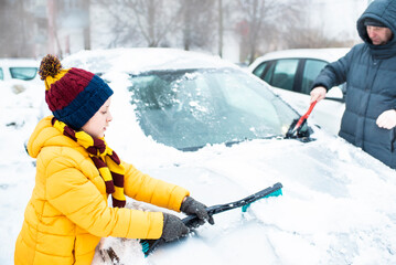 boy helps dad to clear snow from car in winter