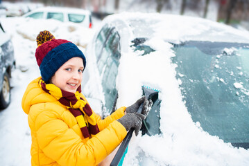 the boy helps his parents remove snow from the windshield of the car. Clear car window in winter...