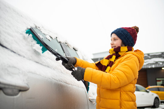 The Boy Helps His Parents Remove Snow From The Windshield Of The Car. Clear Car Window In Winter From Snow In Winter.