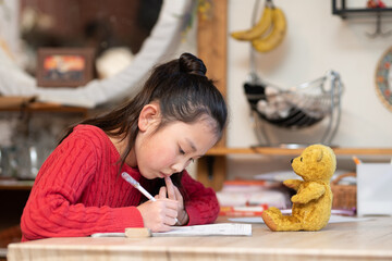 勉強をする女の子と見守る熊の縫いぐるみ