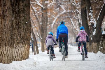 Father and children ride bicycles in winter. A man with his son and daughter ride bicycles along...