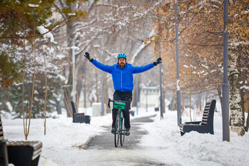 A bearded man rides a bicycle without holding the steering wheel. Biking in the winter park. Active...
