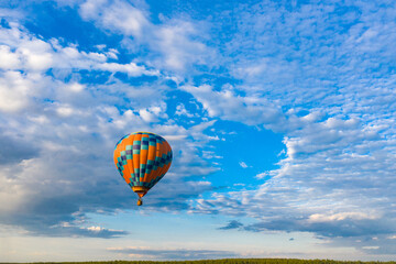 a bright hot air balloon flies against the background of thick clouds and a blue sky