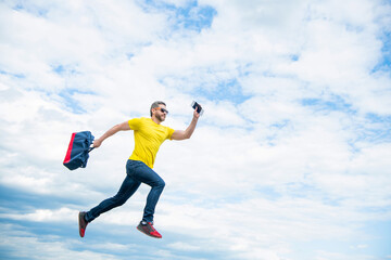 Energetic guy running with travel bag midair sky background, copy space