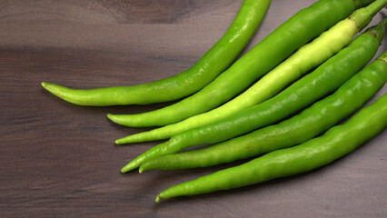 Fresh long Indian green chillies on wooden background.
