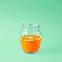 Orange jam. Glass jar with orange juice and slice. Simple sqaure composition on light pastel green background.