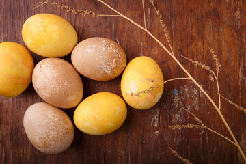 Beautiful Easter eggs colored with natural DIY turmeric and tea paint. Eggs on rustic table with dry branch, top view, close up shot