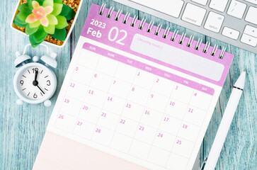 The February 2023 Monthly desk calendar for the organizer to plan 2023 year with alarm clock on wooden table.