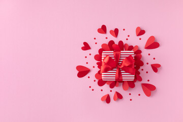 Gift or present box and paper hearts on pink table for Valentine day greeting card. Flat lay style.