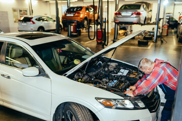 Auto mechanic working with open hood in garage. Repair service concept. Cars on lifts on blurred background.