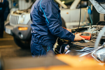 Unrecognizable expertise mechanic working in automobile repair garage. battery inspection. Side...