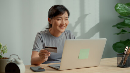 Asian woman holding credit card and using laptop for shopping online.