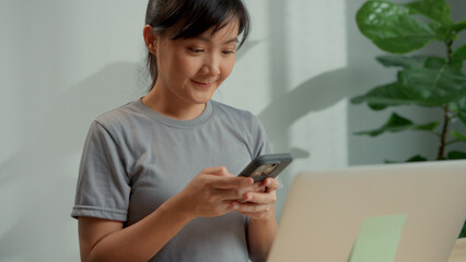 Asian woman happy smiling using smart phone at home office.