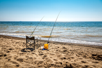 Fototapeta na wymiar Two fishing rods and chair on the beach