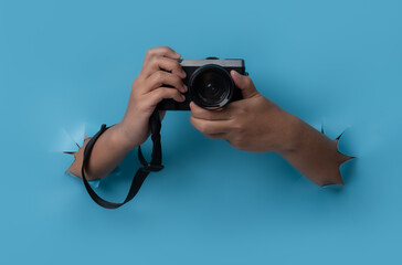 Female hand holding camera breaks through blue paper background.