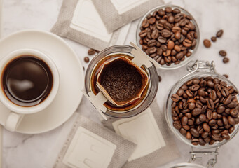 Making drip coffee with a special taste against the background of coffee beans. Drip coffee bag in a coffee cup. Trends in brewing coffee at home.Drip coffee filter. Flatley. Copy space. Place for tex