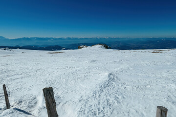 Hiking trail along fence on snow covered hills in winter on Saualpe, Lavanttal Alps, Carinthia, Austria, Europe. Snowcapped mountain ranges of Karawanks and Kamnik Savinja Alps. Winter wonderland