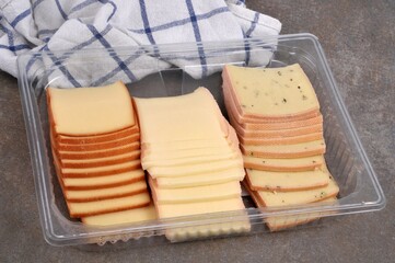 Assortiment de fromages pour raclette dans un emballage plastique avec un torchon sur fond gris