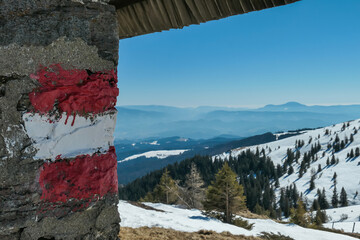 Directional path mark coloured in Austrian flag on the stone wall of a mountain cottage near...