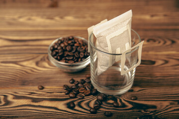 A glass cup of freshly brewed coffee with a handy drip coffee filter on a brown wooden background. Making freshly brewed coffee at home. Copyspace. Place for text.Coffee making concept.