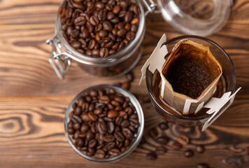 A glass cup of freshly brewed coffee with a handy drip coffee filter on a brown wooden background. Making freshly brewed coffee at home. Copyspace. Place for text.Coffee making concept.