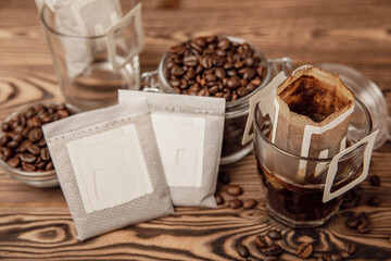 A glass cup of freshly brewed coffee with a handy drip coffee filter on a brown wooden background....