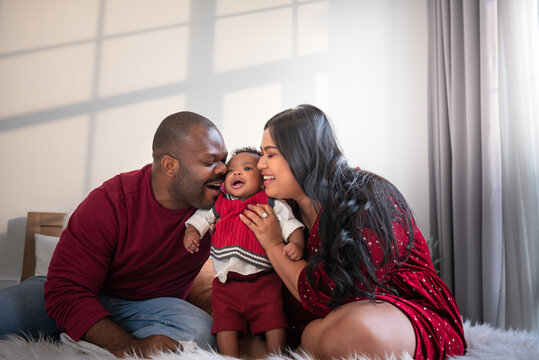 African family, Nigerian father, Asian mother holding and kissing a 4-month-old baby newborn son, they are smile and happy together in bedroom. to African family and baby infant concept.