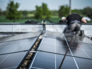 Male team engineers installing stand-alone solar photovoltaic panel system. Electricians mounting blue solar module on roof of modern house. Alternative energy concept