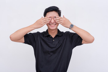 A young asian man covers her eyes with her hands while smiling. Excited and anticipating a happy surprise. Isolated on a white background. Spoiler alert concept.