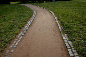 park path made of beige gravel material bordered by granite cubes follow the gravel path with a...
